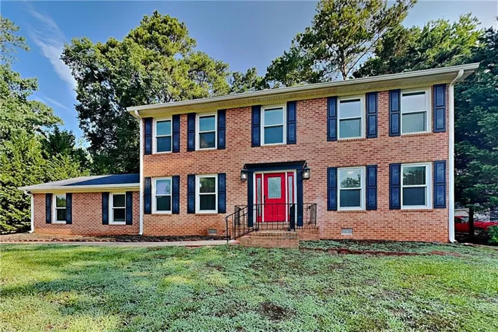 Brick exterior featuring a bright red front door with sidelights, a covered entry, and a dark asphalt shingle roof