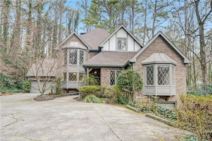Tudor home with a shingled roof, brick siding, concrete driveway, and a garage