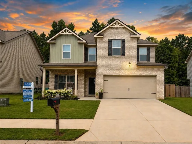 Two-story residence featuring a brick facade with board and batten accents, an attached two-car garage, a covered front porch, a concrete driveway, and a manicured lawn