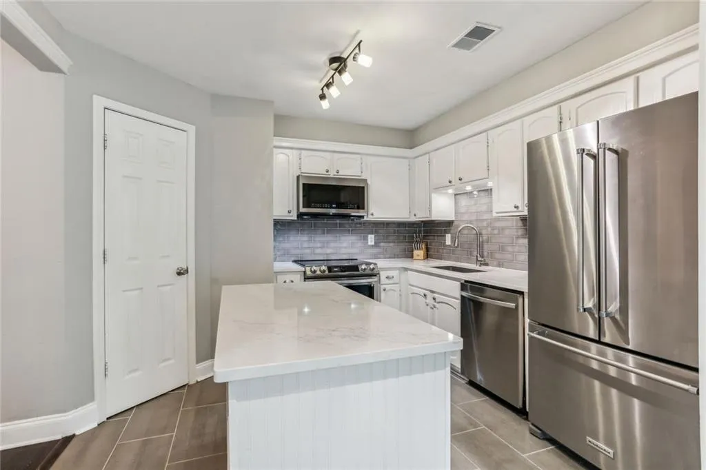 Kitchen with light stone countertops, stainless steel appliances, white cabinetry, and sink Kitchen with light stone countertops, stainless steel appliances, white cabinetry, and sink