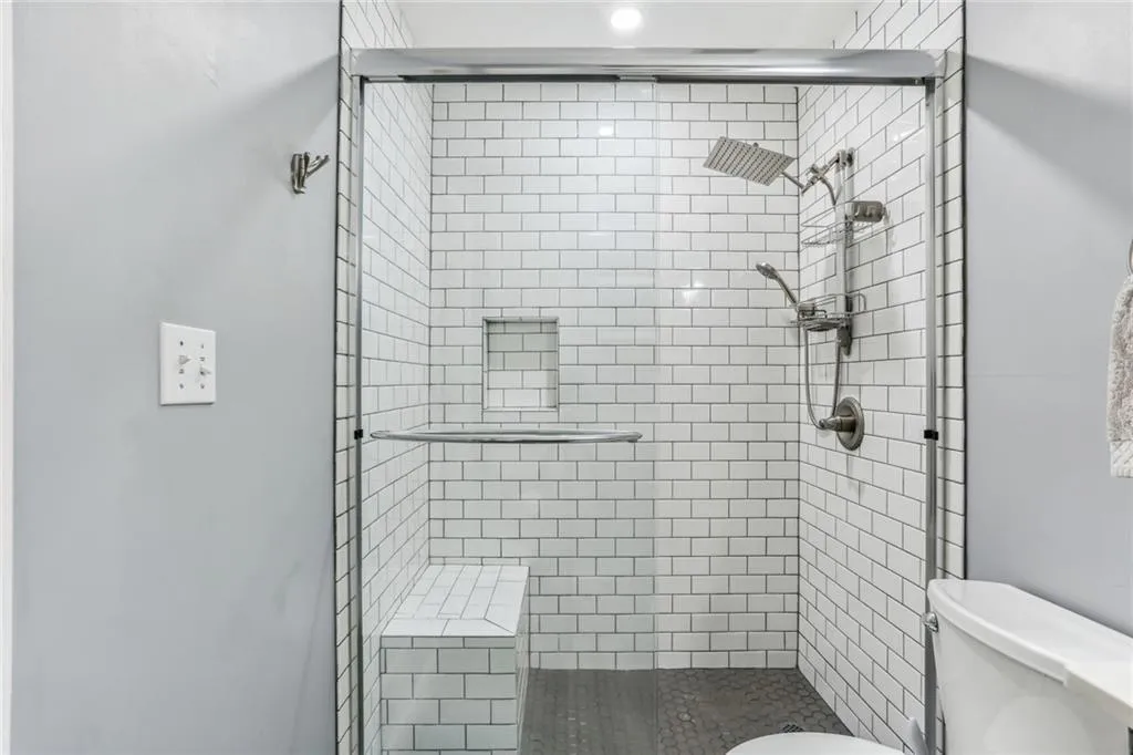 Bathroom featuring an enclosed shower, toilet, and shelves. Bathroom featuring an enclosed shower, toilet, and shelves.