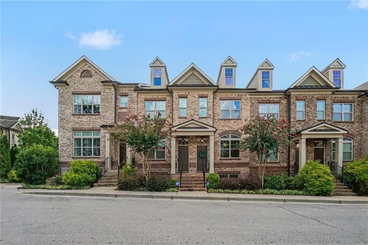 Brick exterior with dormer windows, covered entryways, and mature landscaping