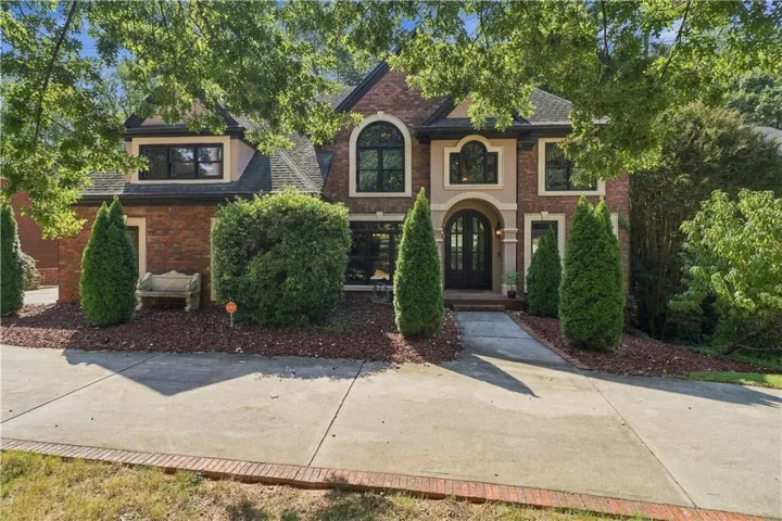 Brick and stucco exterior with arched windows, a covered entry, and a paved driveway