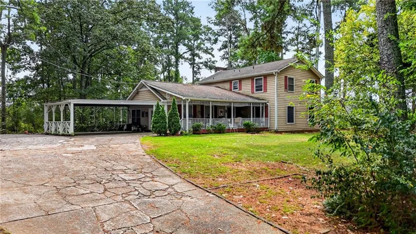 Two-story residence with a covered porch, an attached carport, and mature trees