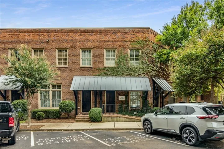 Brick exterior with multiple windows, metal awnings, mature trees, and reserved resident parking