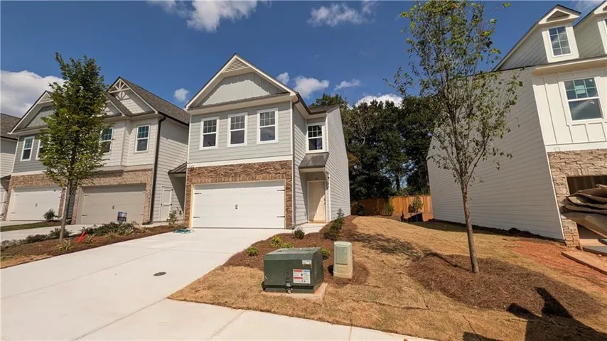 Two-story exterior with light gray siding and stone accents, featuring a two-car garage, a paved driveway, and a landscaped front yard