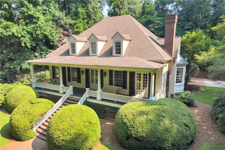 Traditional-style residence featuring a prominent front porch with white columns, a dormer roofline, and dark shutters