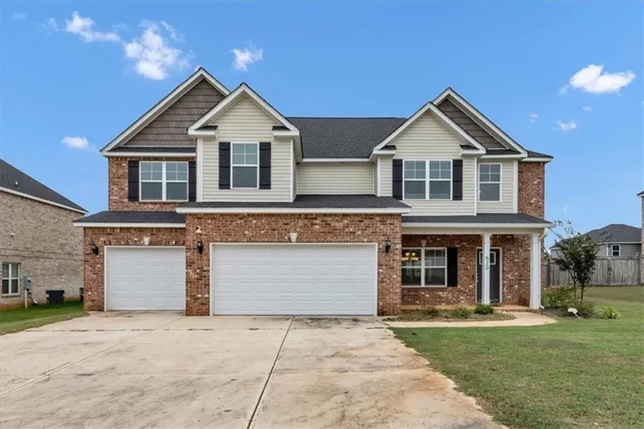 Two-story residence featuring a brick and siding exterior, dual garage doors, a covered entry porch, and a concrete driveway