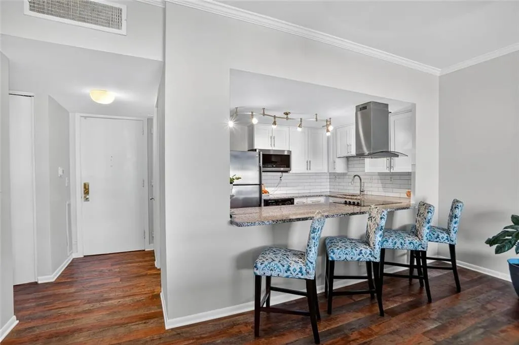 Kitchen featuring dark wood-style flooring, white cabinetry, tasteful backsplash, a kitchen breakfast bar, and stainless steel appliances Kitchen featuring dark wood-style flooring, white cabinetry, tasteful backsplash, a kitchen breakfast bar, and stainless steel appliances