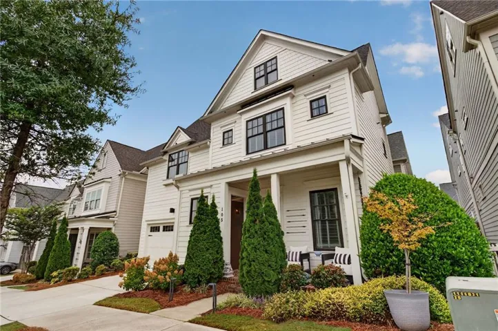 White siding exterior with black-framed windows, a covered front porch, an integrated garage, and professional landscaping