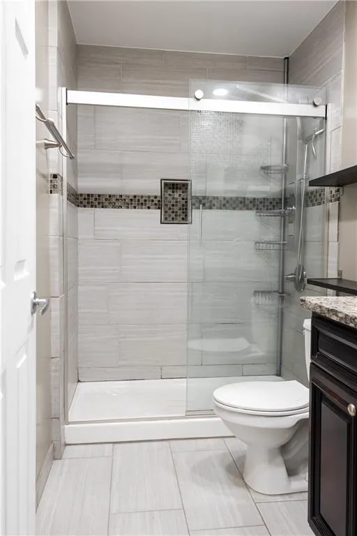 Bathroom featuring vanity, tile flooring, a shower with door, and toilet