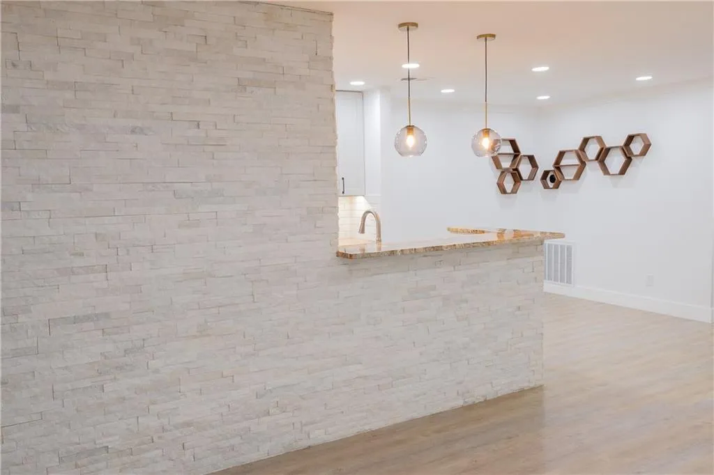 Kitchen featuring kitchen peninsula, hanging light fixtures, white cabinets, light stone countertops, and light wood-type flooring