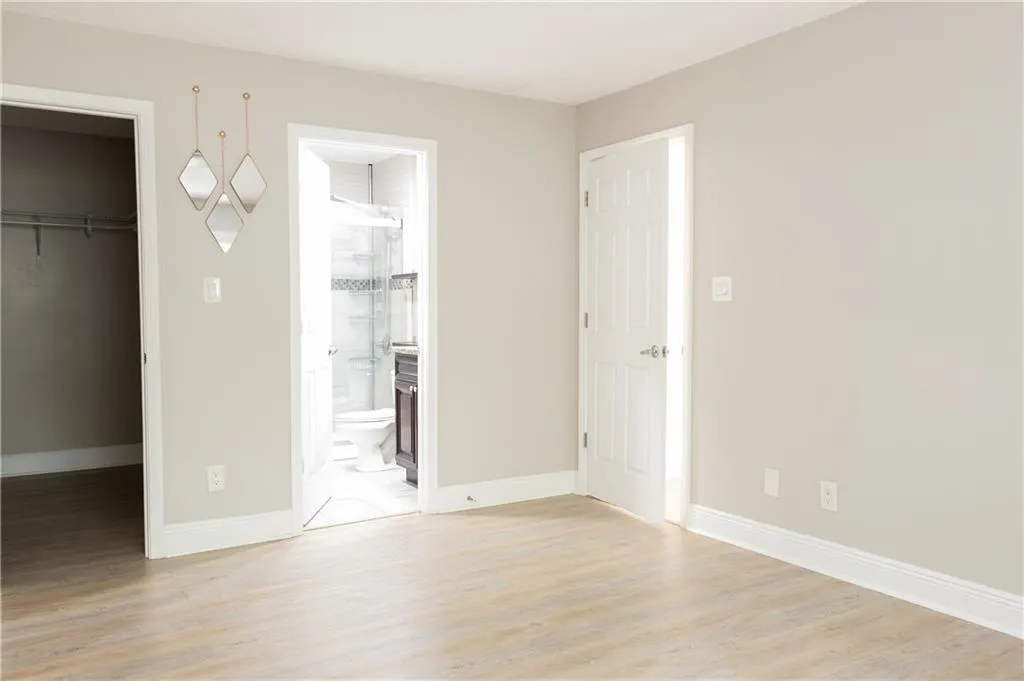 Unfurnished bedroom with ensuite bathroom, a spacious closet, a closet, and light hardwood / wood-style flooring