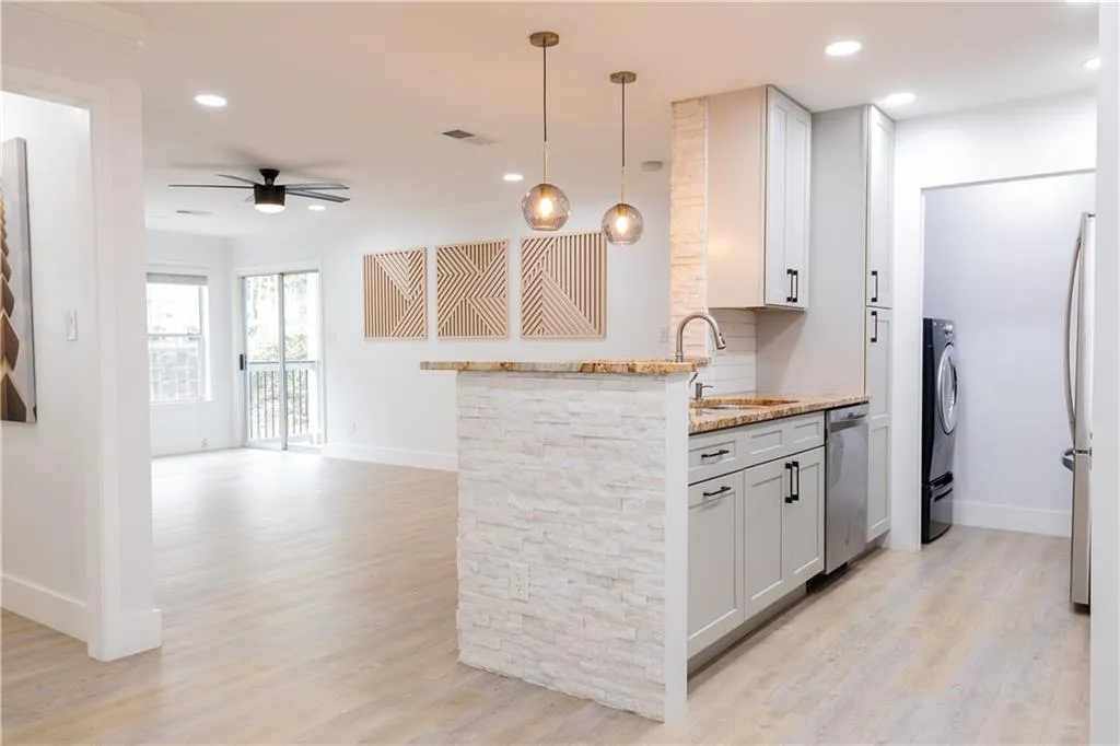 Kitchen with decorative light fixtures, sink, light stone countertops, and light hardwood / wood-style flooring