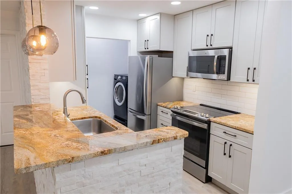 Kitchen featuring sink, washer / dryer, light hardwood / wood-style flooring, stainless steel appliances, and tasteful backsplash