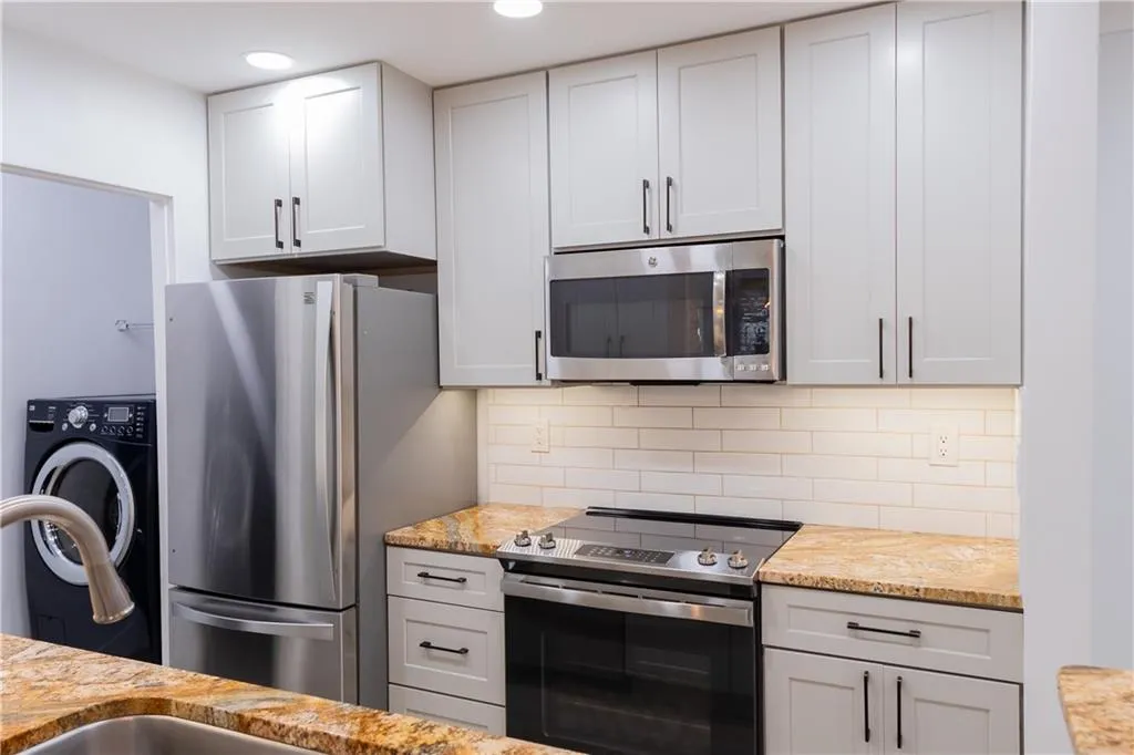 Kitchen featuring tasteful backsplash, white cabinets, appliances with stainless steel finishes, and washer / dryer