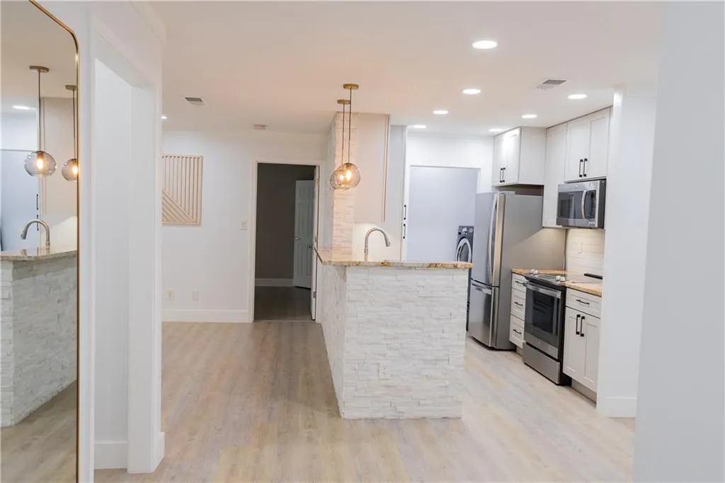 Kitchen with pendant lighting, light hardwood / wood-style floors, light stone countertops, appliances with stainless steel finishes, and white cabinets