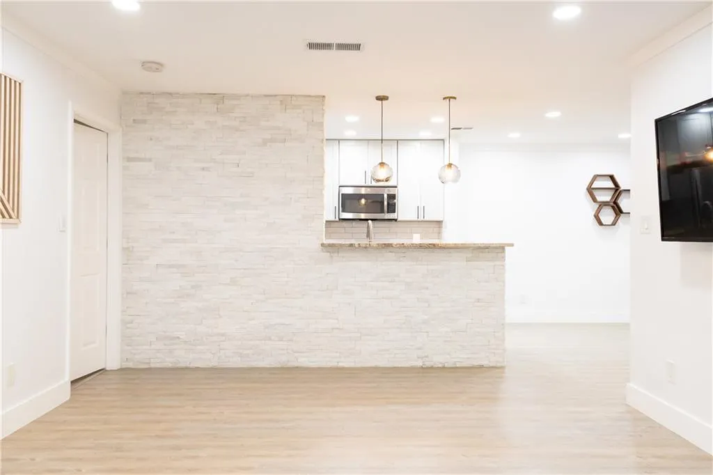 Kitchen with pendant lighting, light hardwood / wood-style floors, light stone countertops, white cabinetry, and crown molding