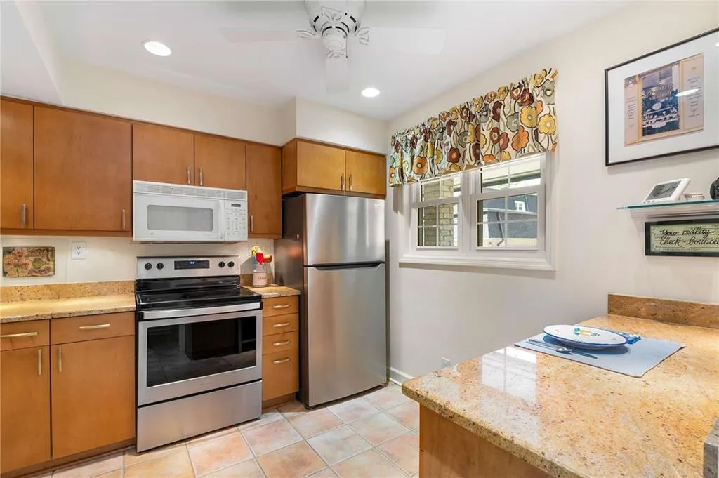 Kitchen with stainless steel appliances, light tile patterned floors, brown cabinets, and a ceiling fan