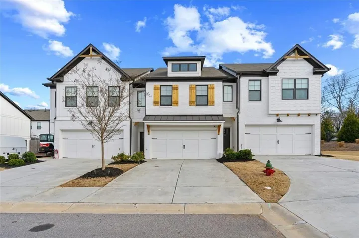 Modern townhome exterior featuring white brick and siding, black-framed windows, wood-tone decorative shutters, and individual attached garages