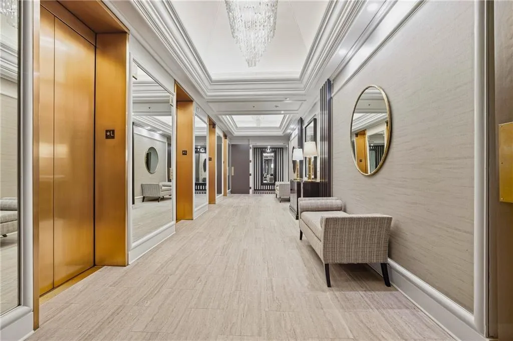 Hallway with wood-finish flooring, gold-toned elevator doors, mirrored wall panels, and a decorative oval mirror