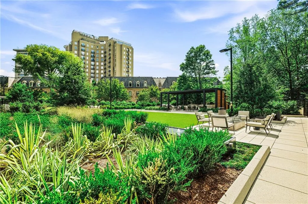 Expansive outdoor common area featuring a manicured lawn, a modern pergola, a paved patio, and mature trees
