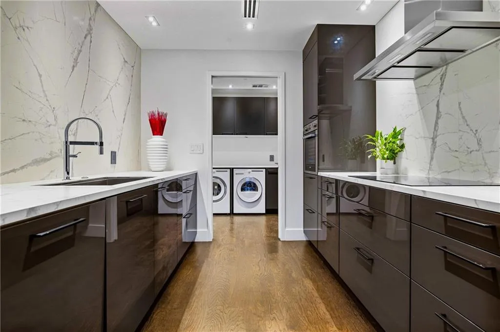 Galley kitchen featuring glossy dark cabinetry, stone countertops, a large single-basin sink, and integrated appliances