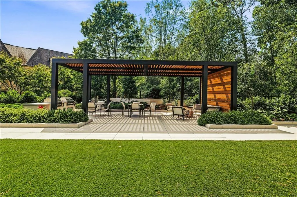 Expansive outdoor living area featuring a modern pergola with a slatted wood roof, a built-in outdoor kitchen with grill, and a surrounding concrete patio