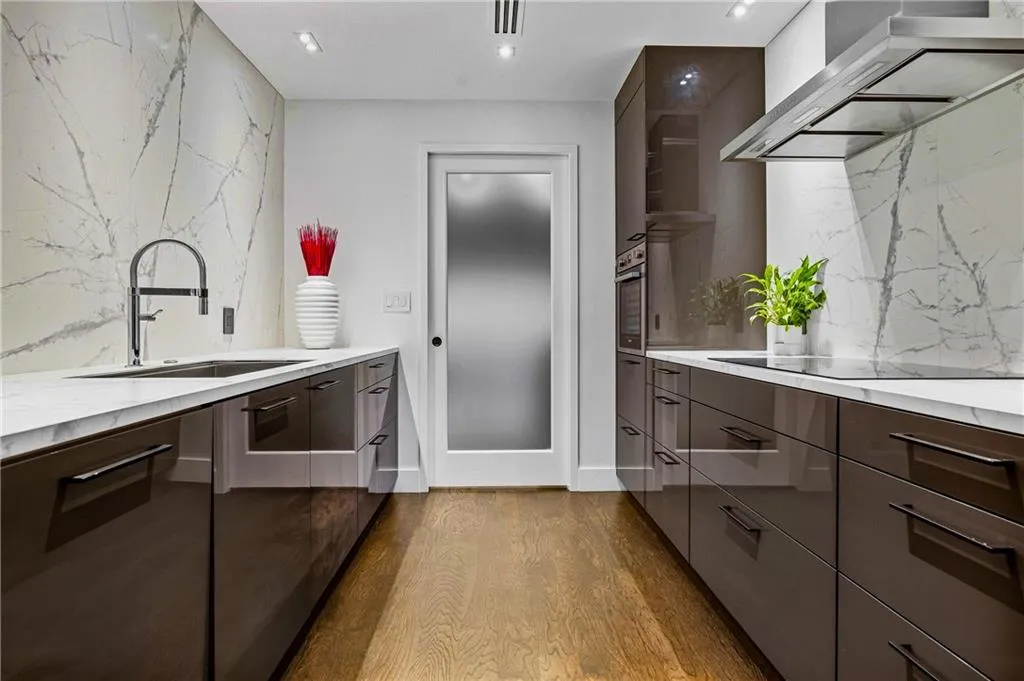 Gourmet kitchen featuring high-gloss cabinetry, integrated stainless steel appliances, a range hood, and a full-height stone backsplash with coordinating countertops