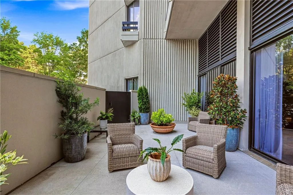 Private outdoor patio space featuring concrete flooring, a solid privacy wall, and floor-to-ceiling windows with integrated louvered panels