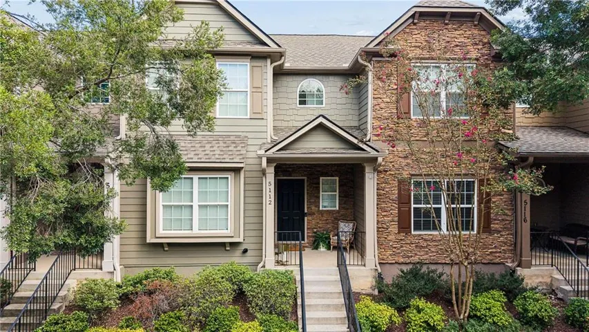 Stone veneer and siding facade, covered entry, front porch with black railing, multiple windows with shutters, and mature landscaping