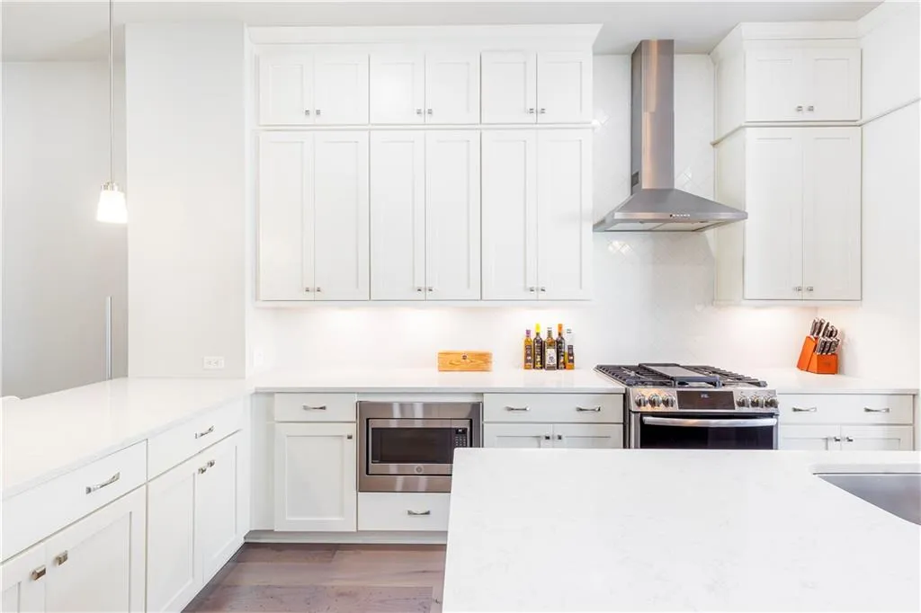 Kitchen with wall chimney range hood, stainless steel appliances, and white cabinets