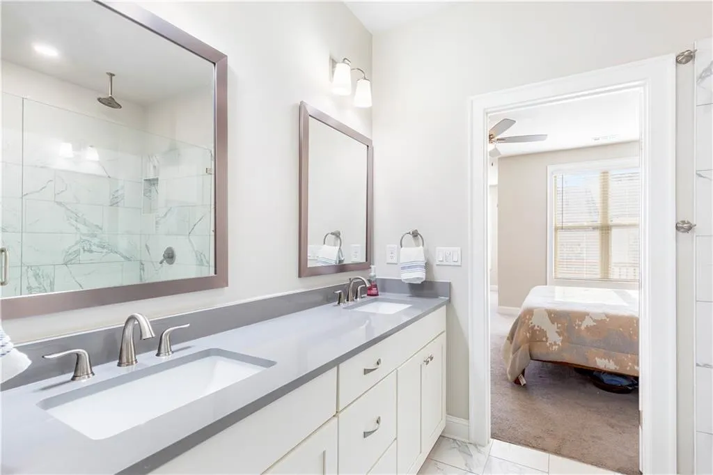 Full bath featuring double vanity, light marble finish floors, a marble finish shower, and ensuite bath