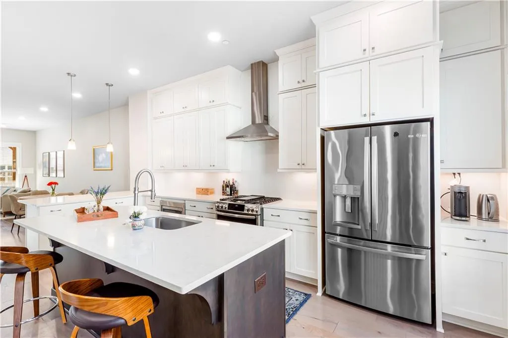 Kitchen with stainless steel appliances, wall chimney exhaust hood, an island with sink, a kitchen bar, and decorative light fixtures