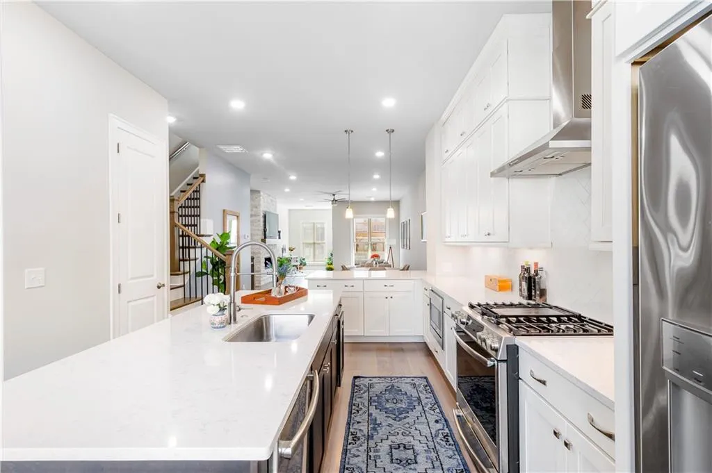 Kitchen featuring white cabinets, stainless steel appliances, a center island with sink, recessed lighting, and wall chimney range hood