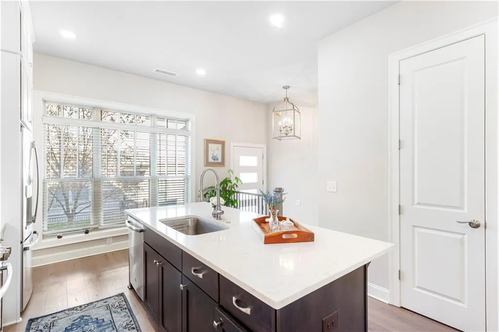 Kitchen with dark brown cabinetry, pendant lighting, light stone counters, light wood-style floors, and a kitchen island with sink