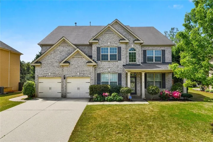 Two-story brick exterior featuring a covered front entry, arched windows, and a two-car garage with carriage-style doors