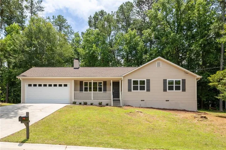Ranch-style residence featuring a two-car garage, covered porch with white railings, and mature trees providing a natural backdrop
