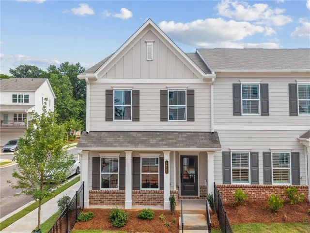 Contemporary townhome exterior featuring light-colored siding, a prominent gable, dark functional shutters, and a brick foundation accent