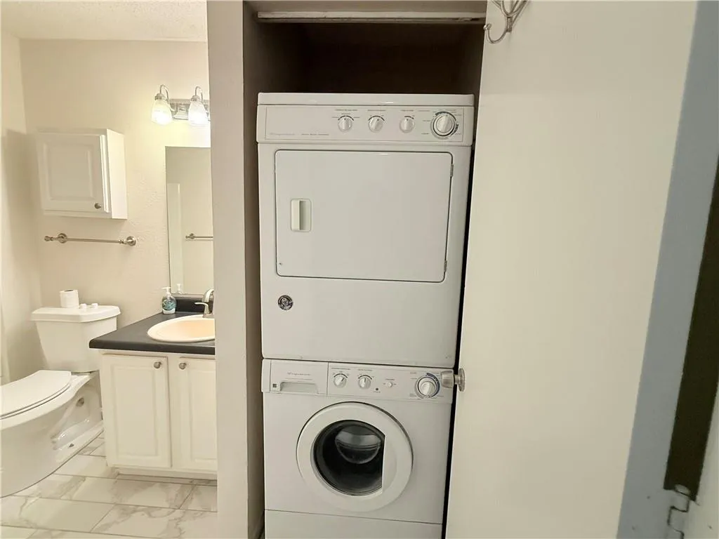 Laundry room featuring light marble finish floors, stacked washing machine and dryer, and a textured ceiling