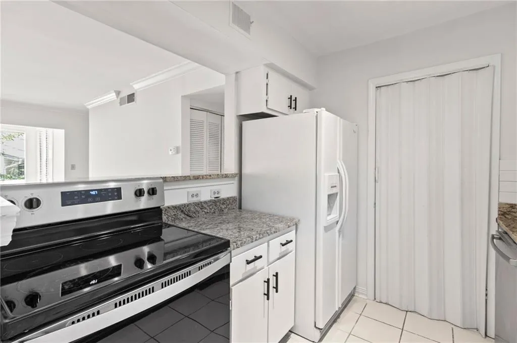Kitchen with light tile patterned flooring, appliances with stainless steel finishes, white cabinetry, ornamental molding, and light stone countertops