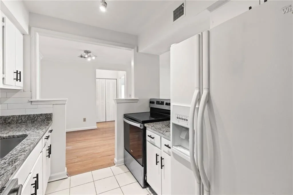 Kitchen featuring stainless steel electric range oven, white cabinets, white refrigerator with ice dispenser, light tile patterned floors, and light stone counters