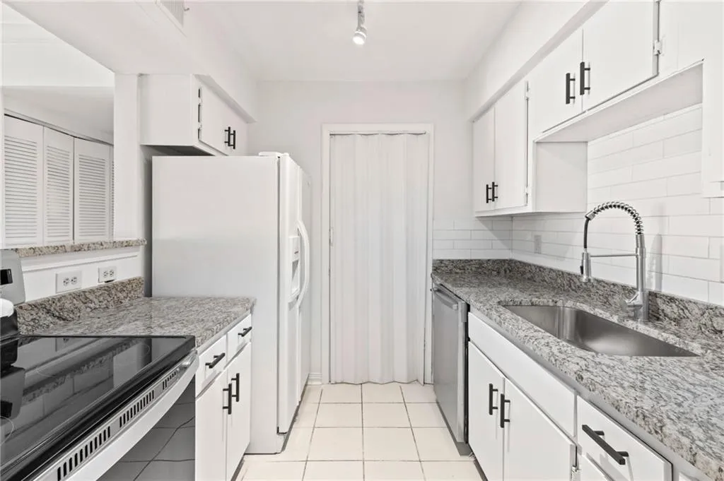 Kitchen with sink, light tile patterned floors, backsplash, stainless steel appliances, and white cabinets