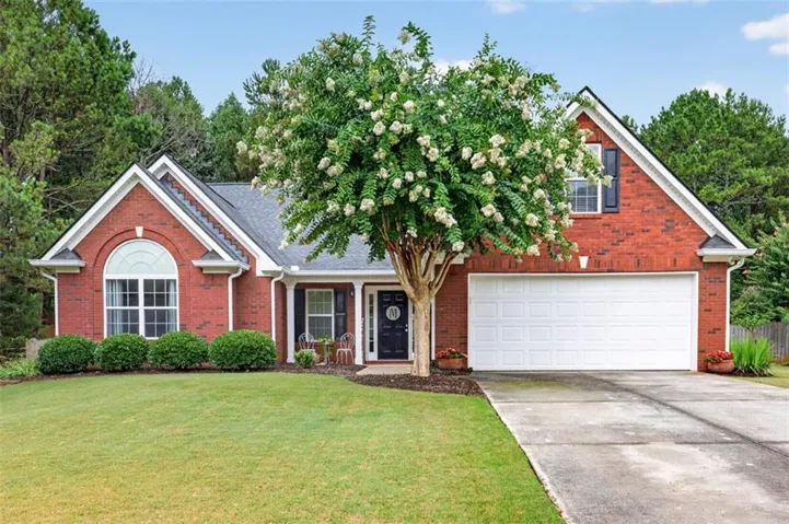 Brick facade residence featuring a two-car garage, established front lawn, mature flowering tree, and a covered porch