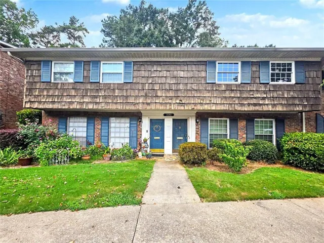 Brown cedar shake siding with brick detailing, blue shutters, and a central sidewalk leading to twin blue entry doors