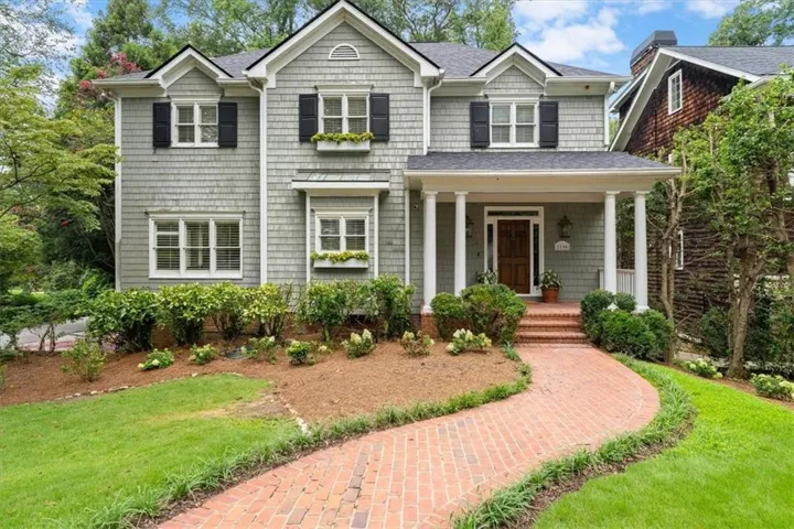 Shingle-sided exterior with black window shutters, a covered front porch with white columns, and a brick pathway