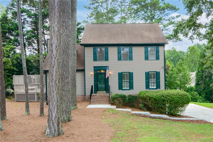 Two-story residence featuring a brick entryway, dark green shutters, and a rear elevated deck