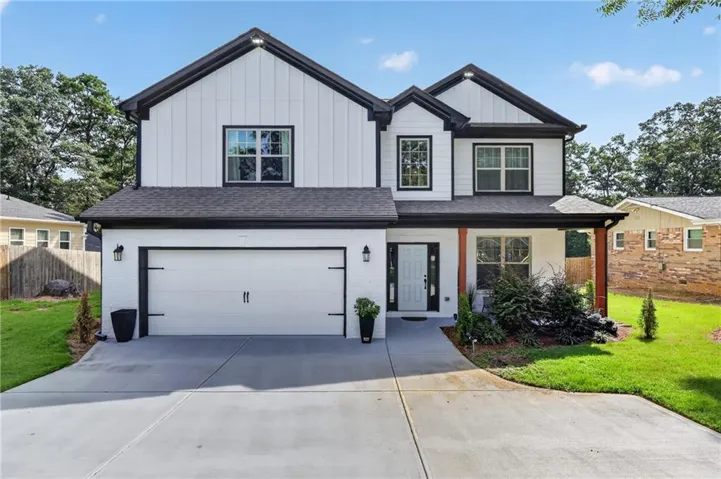 Modern farmhouse-style exterior featuring white board-and-batten siding with black trim, a dark gray shingle roof, a two-car garage with carriage-style doors, a covered porch with natural wood columns, and a concrete driveway