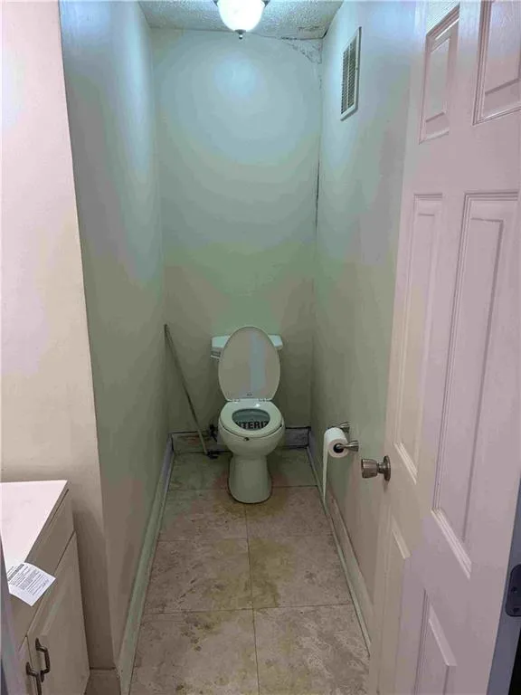 Another view of the half bathroom with light tile patterned floors and a textured ceiling.
