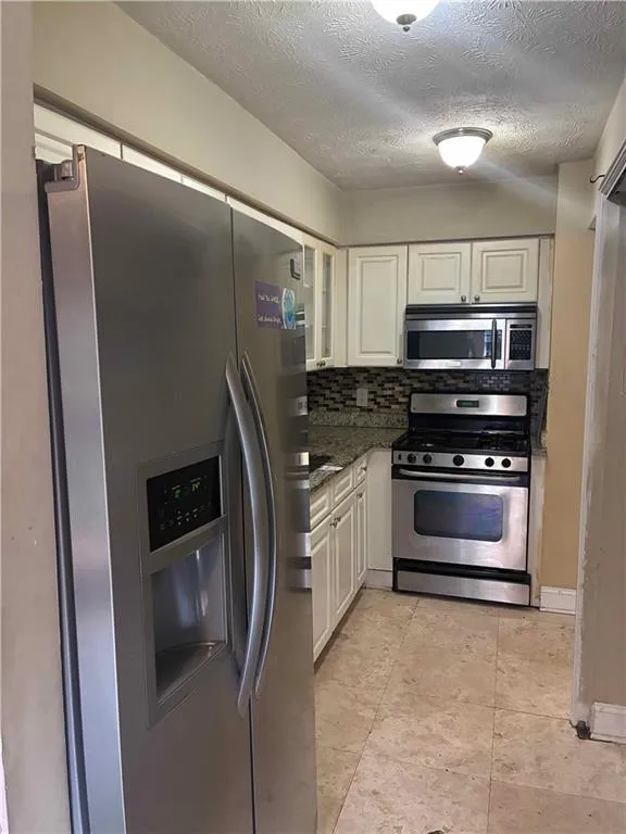 Kitchen with stainless steel appliances, backsplash, dark stone countertops, a textured ceiling, and white cabinetry